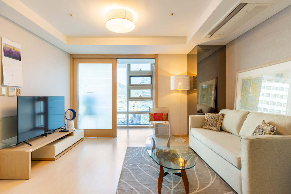 Modern living room with a sofa, glass table, and large window overlooking the city.
